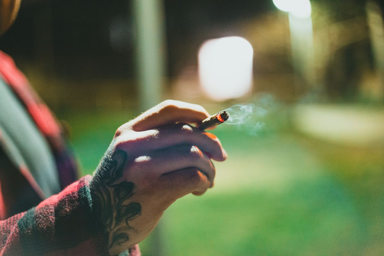 close up of a tattooed hand holding a lit joint outdoors at night with