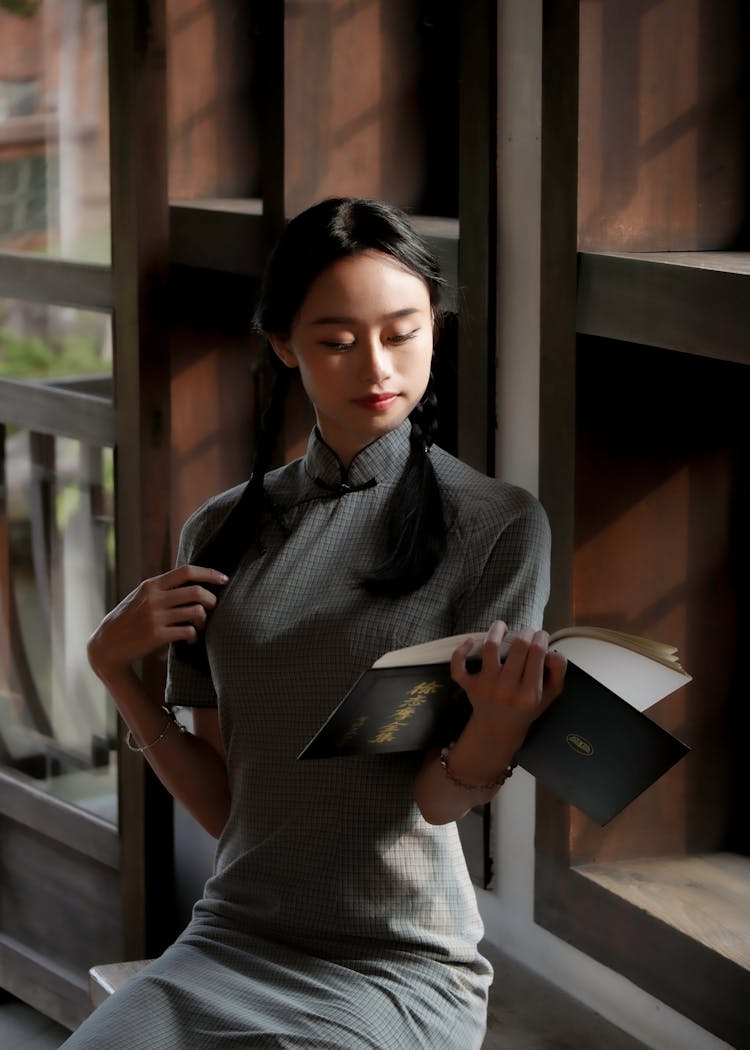 A Woman In A Cheongsam Reading A Book Indoors