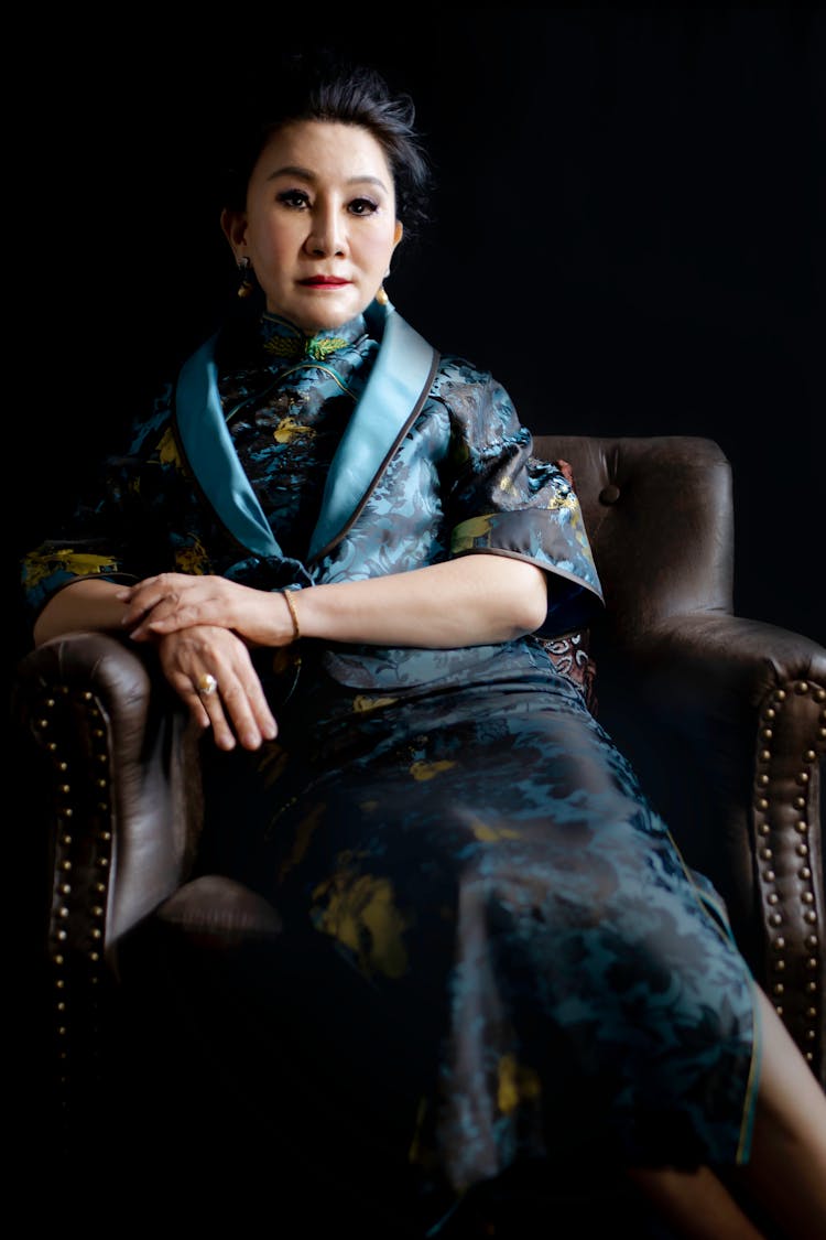 A Woman In A Cheongsam Sitting In An Armchair