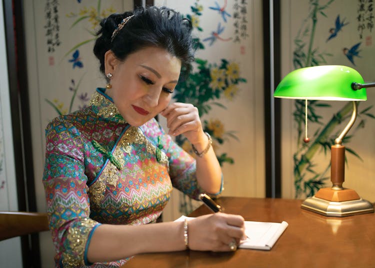  A Woman In A Cheongsam Writing On A Table