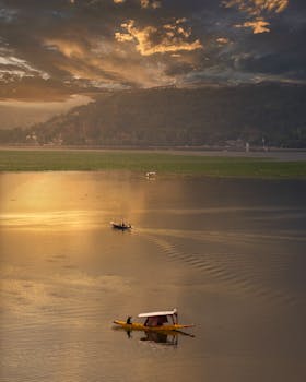 A tranquil scene of a boat at sunset on Dal Lake, surrounded by serene waters and majestic mountains.