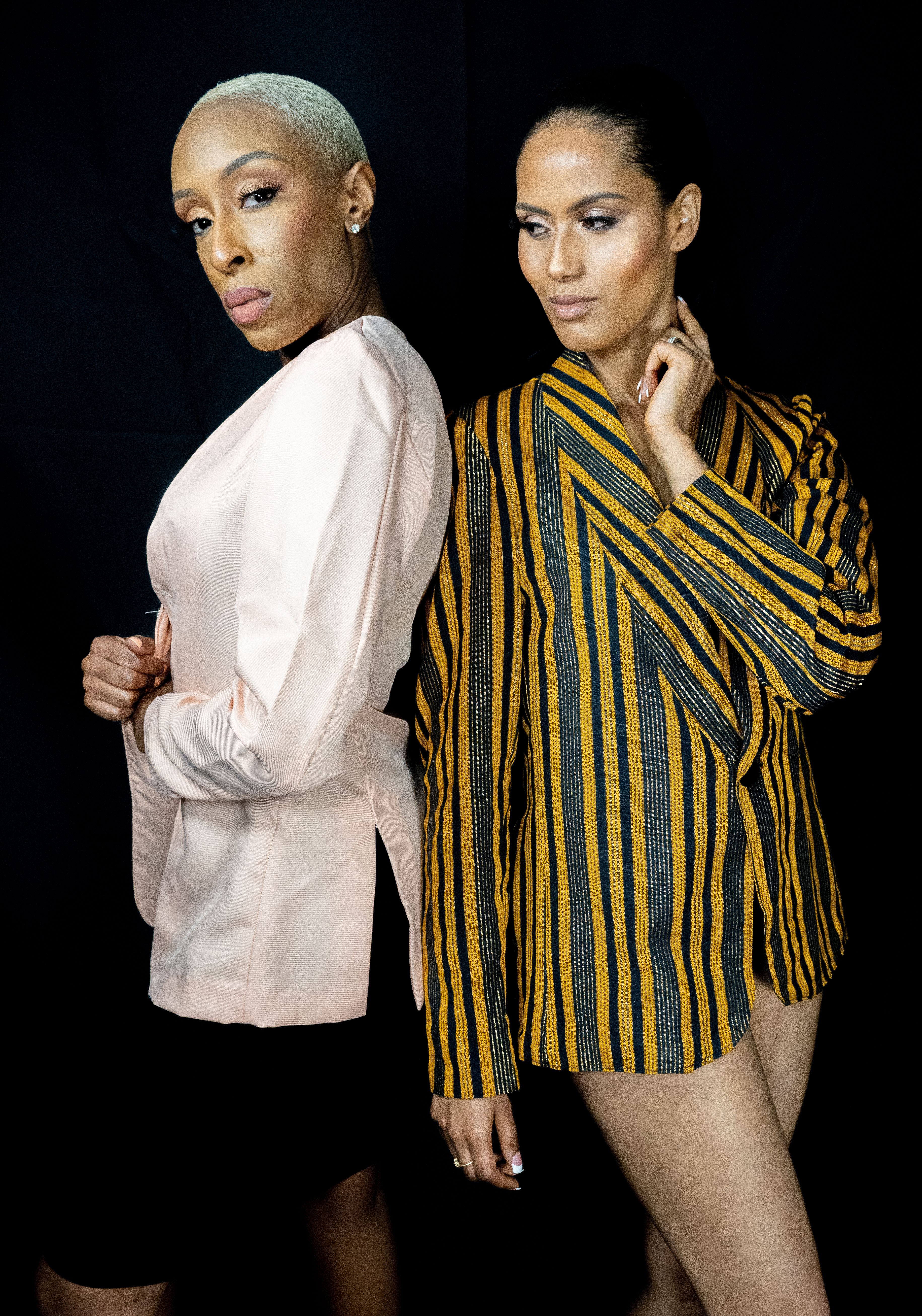 Elegant portrait of two black fashion models posing stylishly in a studio with distinct outfits and a black background.