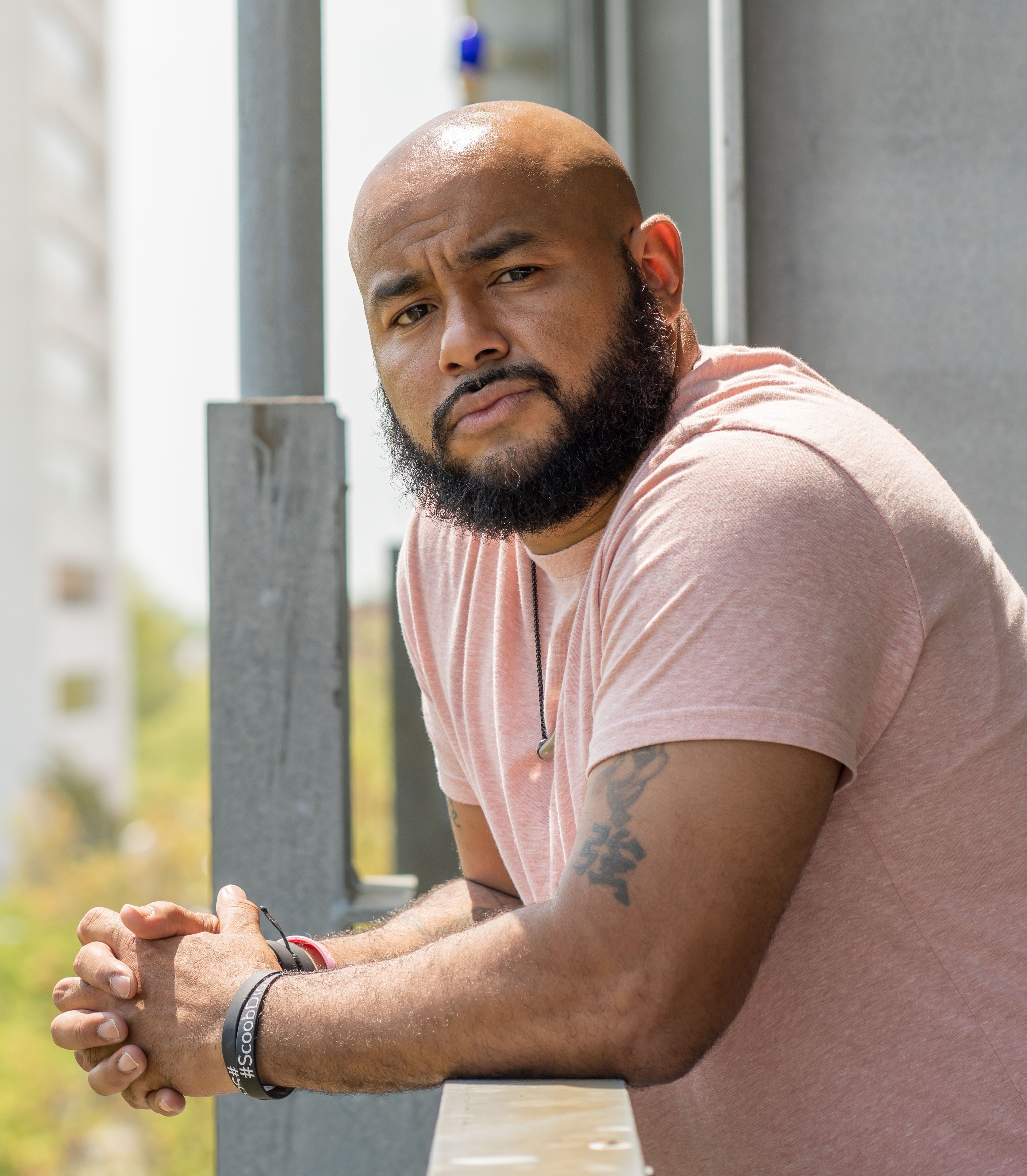 A serious bearded man in a pink shirt leaning on a balcony in Columbia, MD.