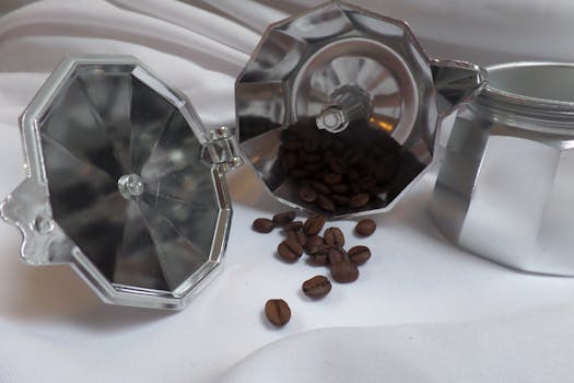 A detailed still life of coffee beans spilling from a moka pot on a white cloth, highlighting morning coffee rituals.