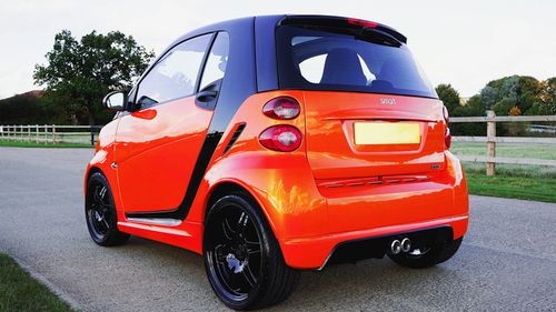 Free A vibrant orange Smart car is parked on a road in Knebworth, showcasing its sleek design. Stock Photo