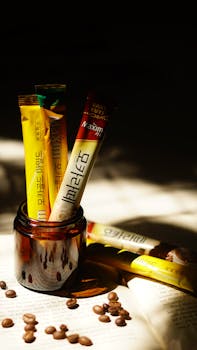 A close-up of coffee sachets in a glass container surrounded by coffee beans on an open book.
