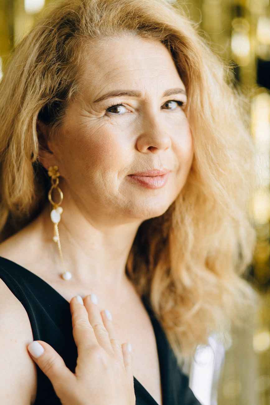 Charming portrait of a smiling middle-aged woman with blonde hair in a stylish black top.
