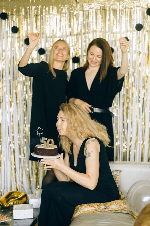 Free Three women celebrating a 50th birthday with cake and decorations, showcasing joy and friendship indoors. Stock Photo