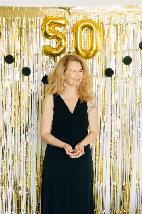 Free Smiling woman in a black dress celebrates her 50th birthday with golden decorations inside. Stock Photo