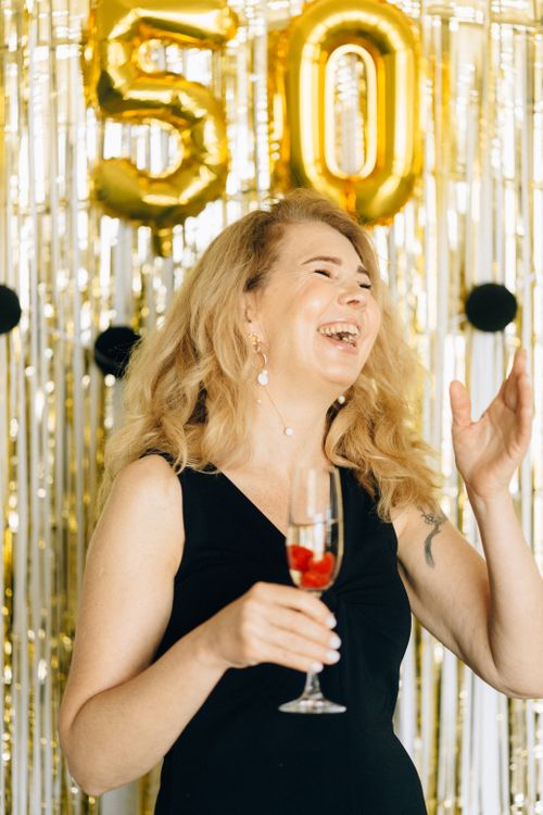 Free Woman joyfully celebrating her 50th birthday with champagne and balloons. Stock Photo