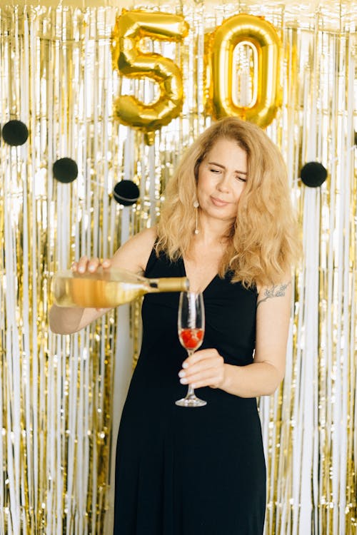 Woman in Black Sleeveless Dress Pouring Champagne in a Glass