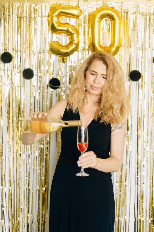Free Woman in black dress pouring champagne under golden 50 balloons. Stock Photo