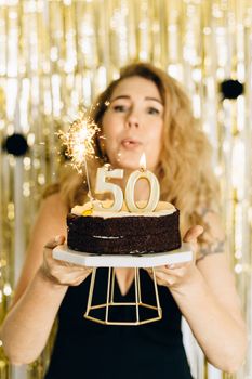 Woman holding cake with '50' candles and sparklers for birthday celebration.