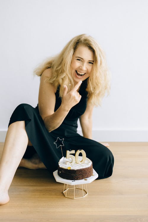 A Happy Woman Sitting on the Wooden Flooring Near the Stand with Cake