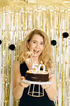 Woman joyfully holding a chocolate birthday cake with gold candles celebrating a 50th birthday.