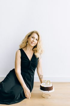 A joyful woman in an elegant dark dress celebrating her 50th birthday indoors with a cake.