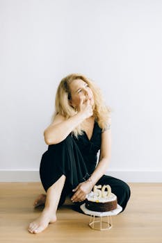 A woman wearing a black dress celebrates her 50th birthday with a cake indoors.