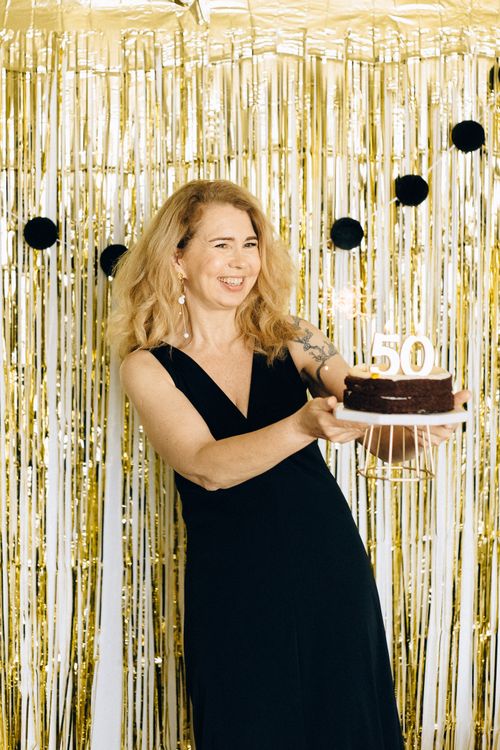 Free Woman celebrating her 50th birthday with a cake in an elegant setting. Stock Photo