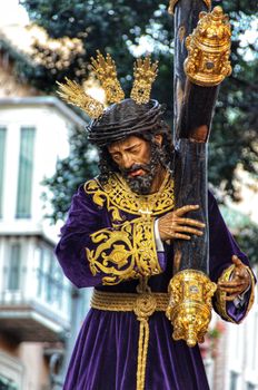A detailed statue of Jesus in a traditional religious procession, adorned with gold and purple robes.