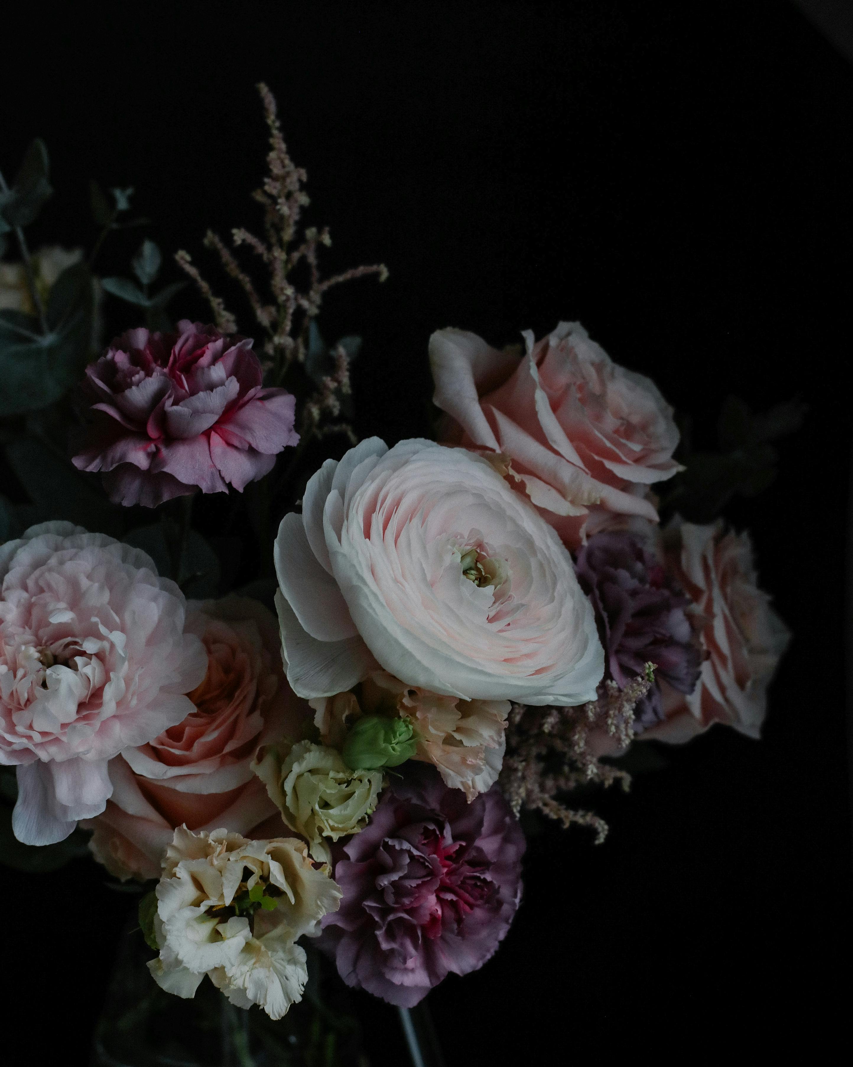 Stunning bouquet of roses, ranunculus, and carnations arranged artfully against a dark backdrop.