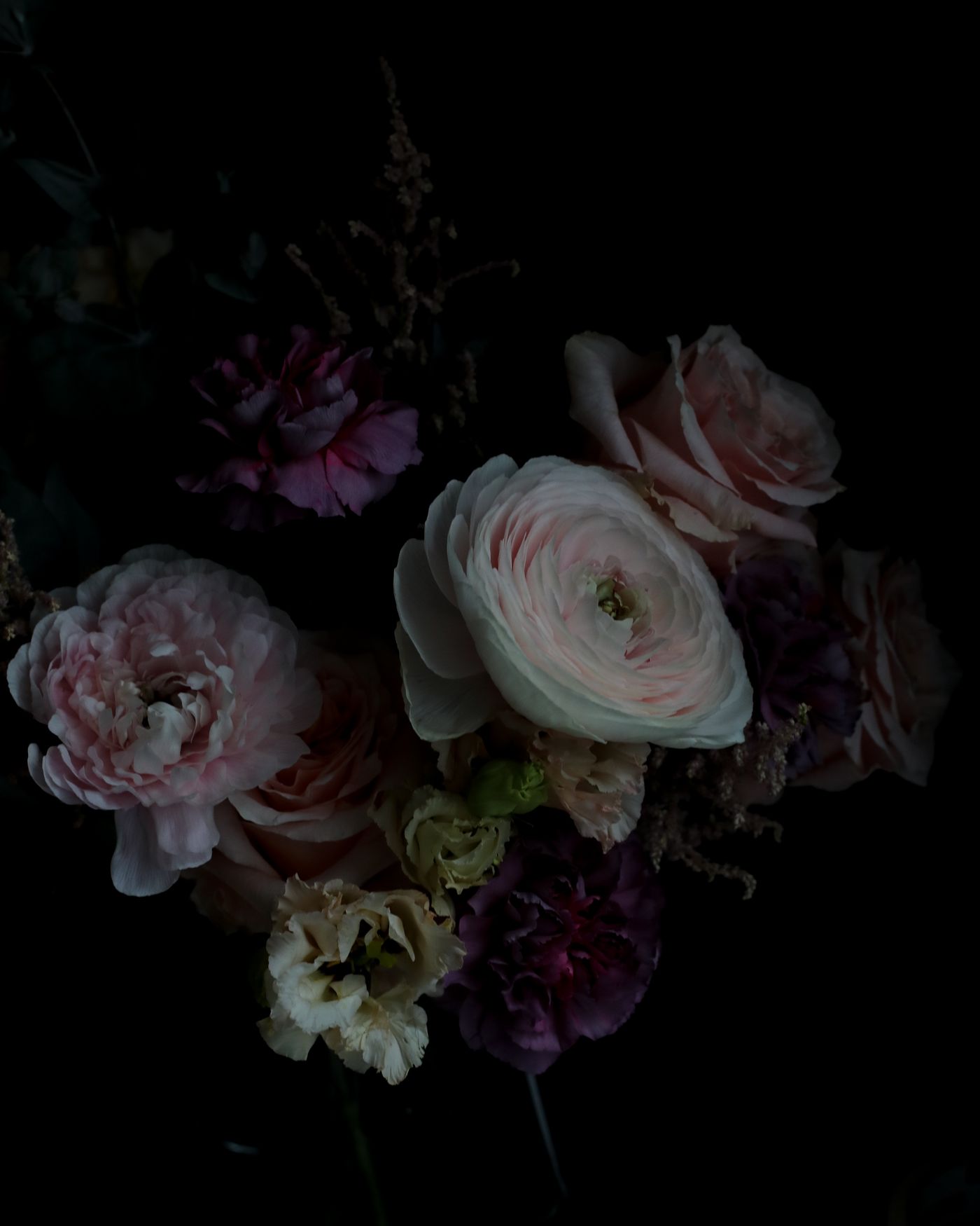 A dark, romantic arrangement of pale ranunculus and garden roses