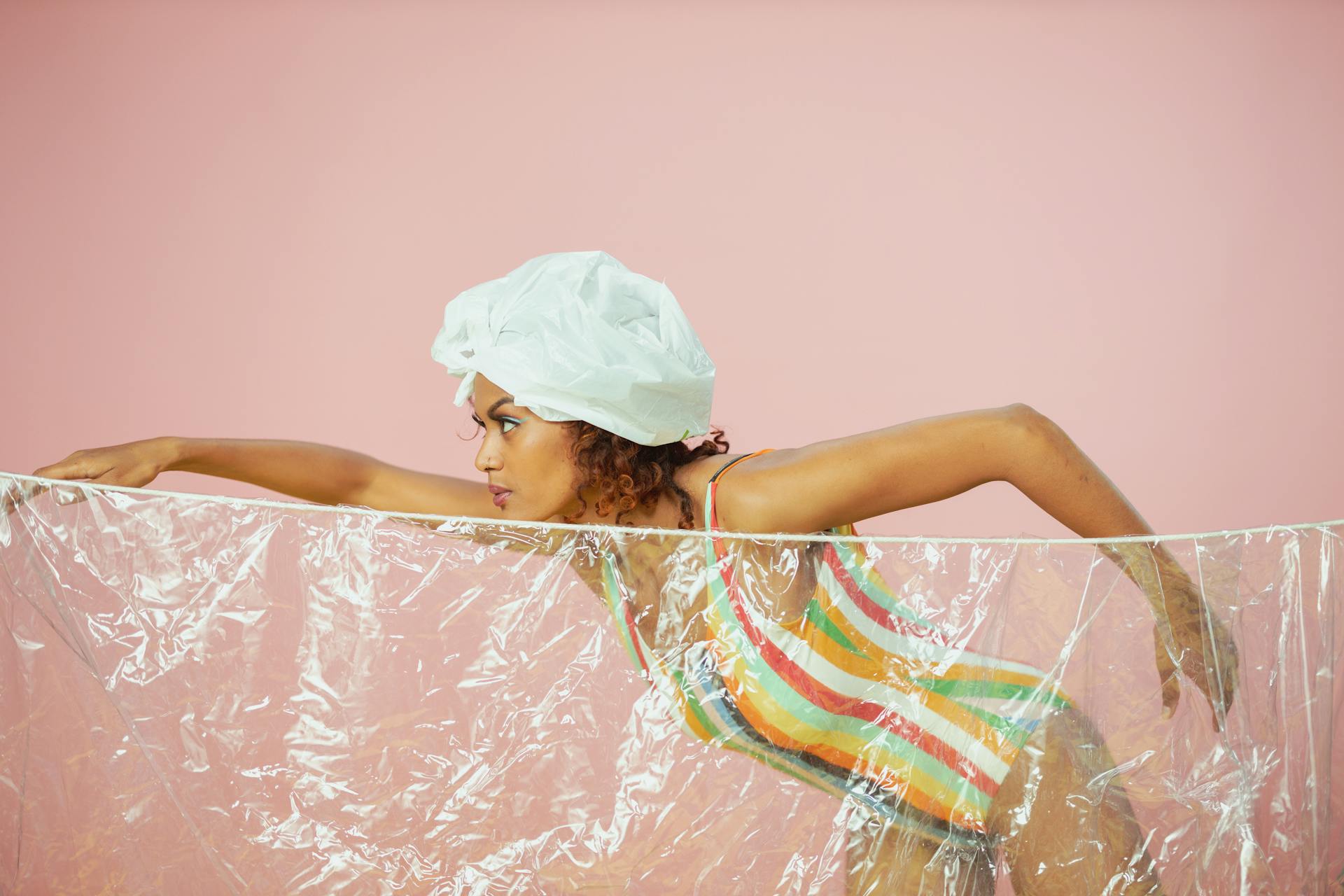 Artistic studio shot of a woman posing with plastic wrap, emphasizing fashion and recycling themes.