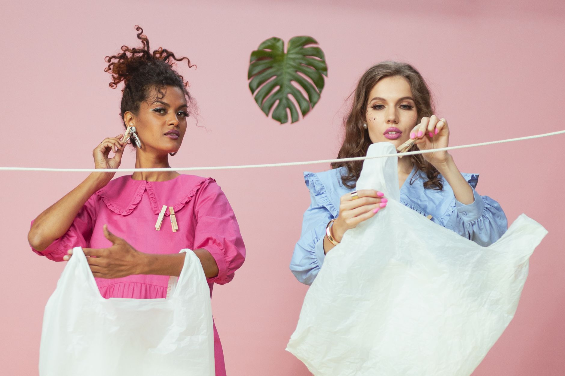 Two women hanging recycled plastic bags on a clothesline in a studio setting.