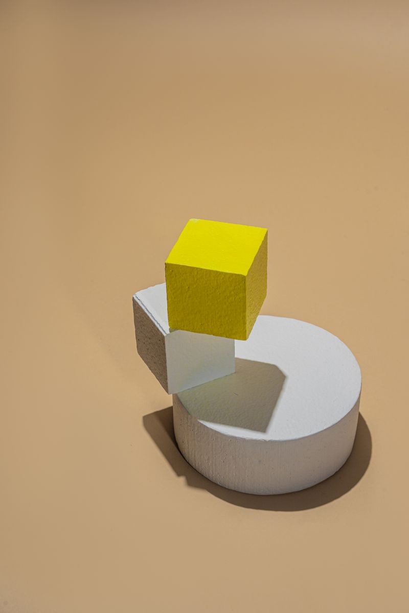 Abstract composition with geometric shapes and vibrant yellow cube on neutral background.