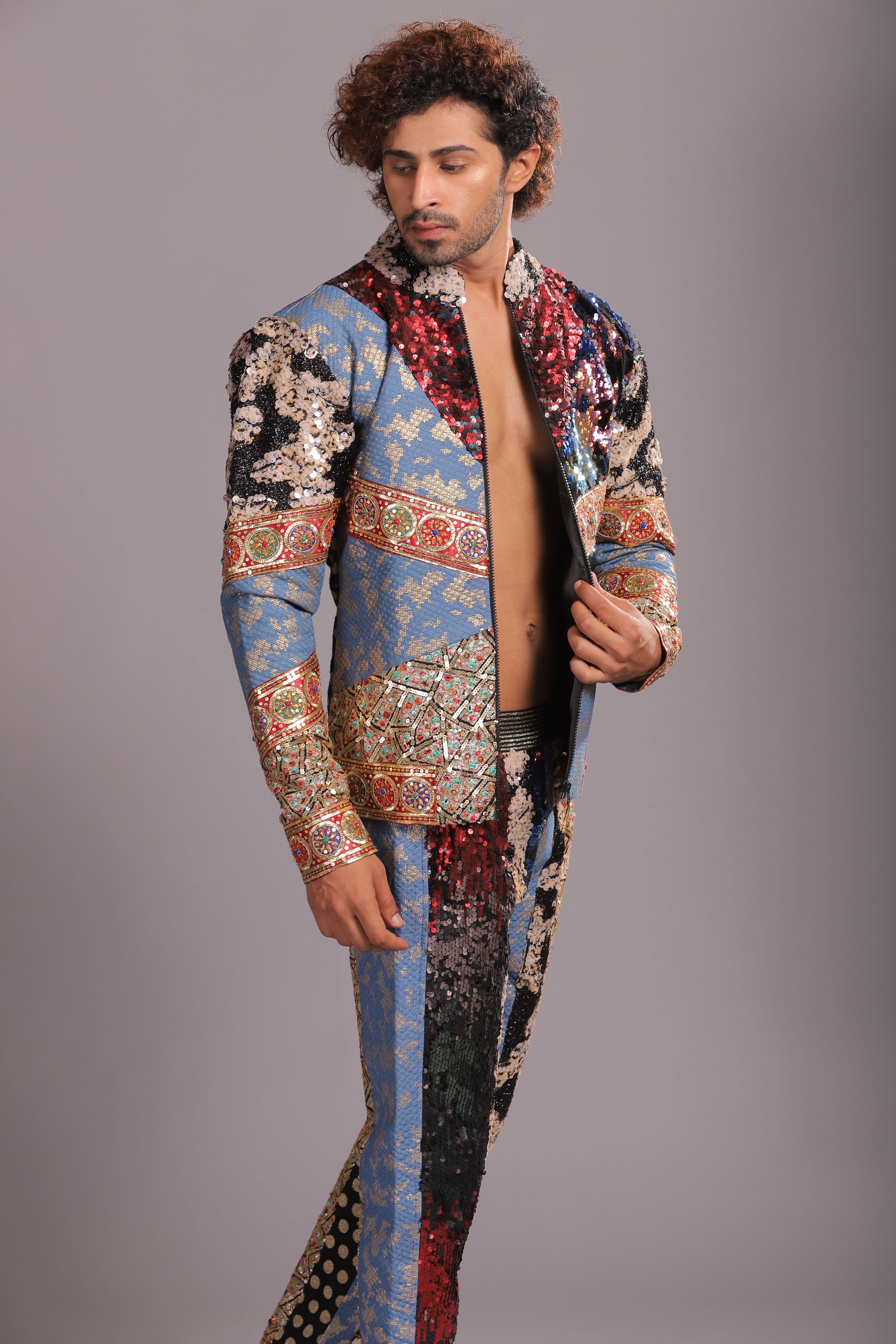 A fashionable man with curly hair looks over his shoulder wearing a vibrant printed outfit in a photoshoot.
