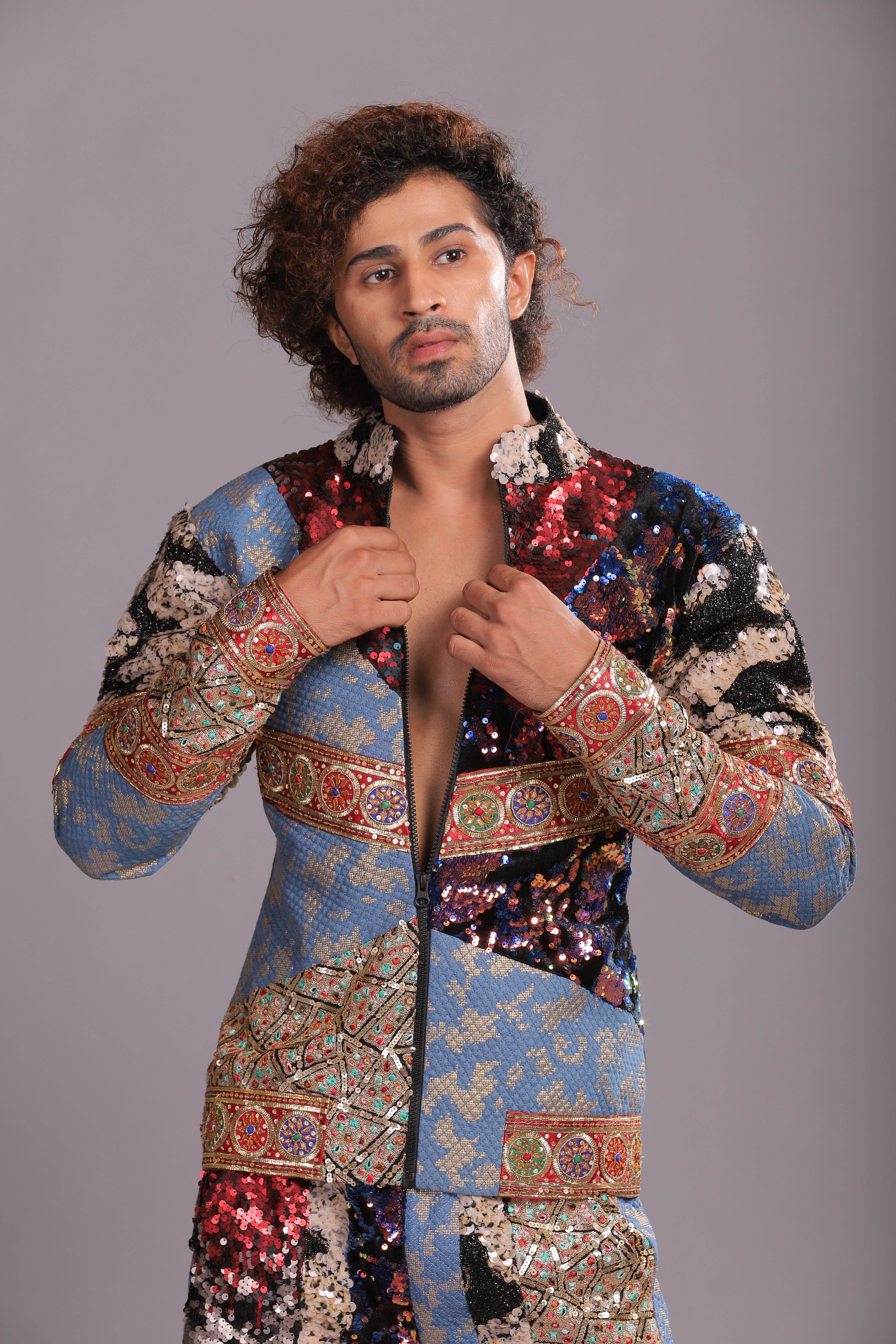Young man wearing a colorful, sequined outfit, showcasing bold fashion in a studio setting.