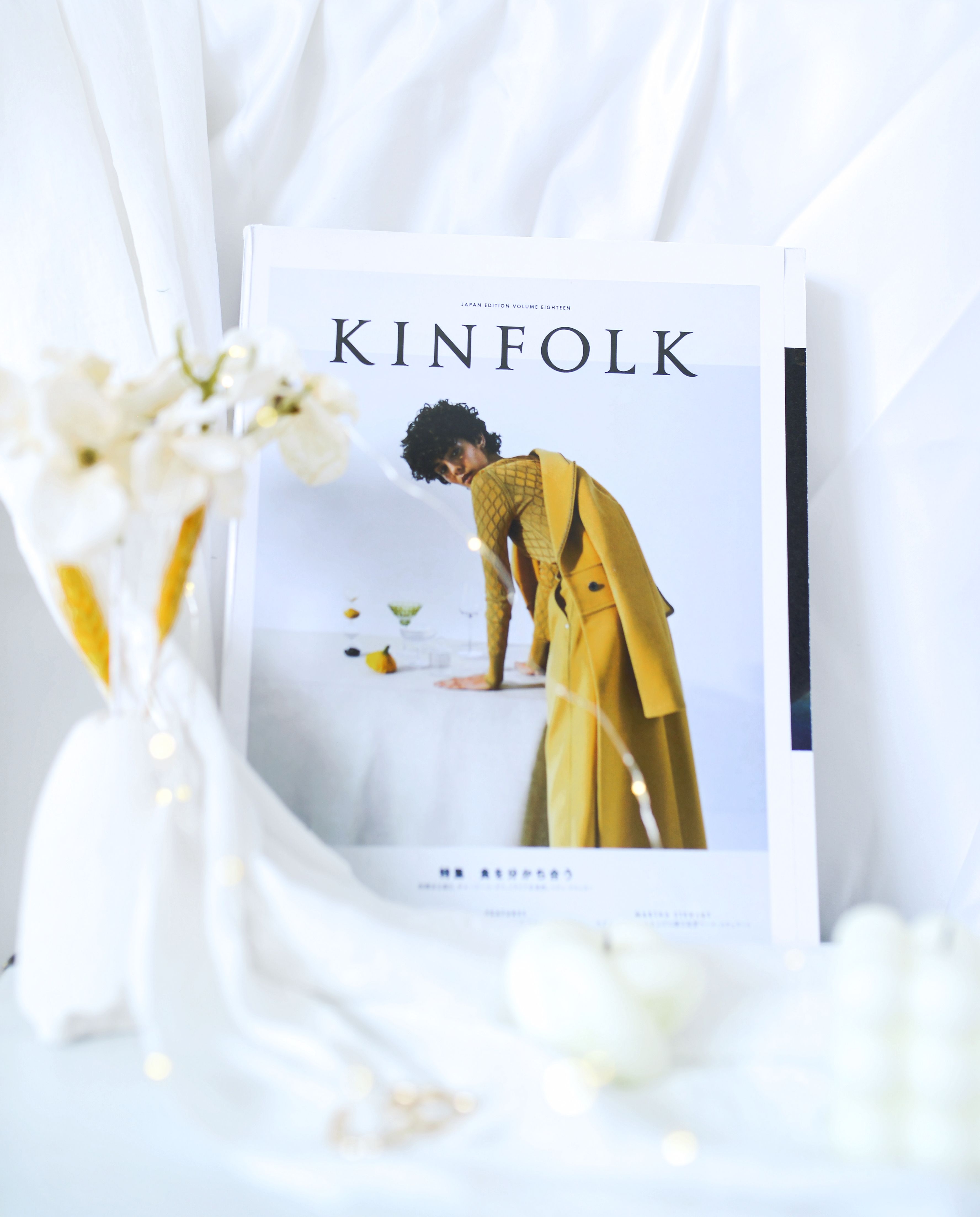 Stylish magazine cover resting on white cloth with elegant flowers in foreground.
