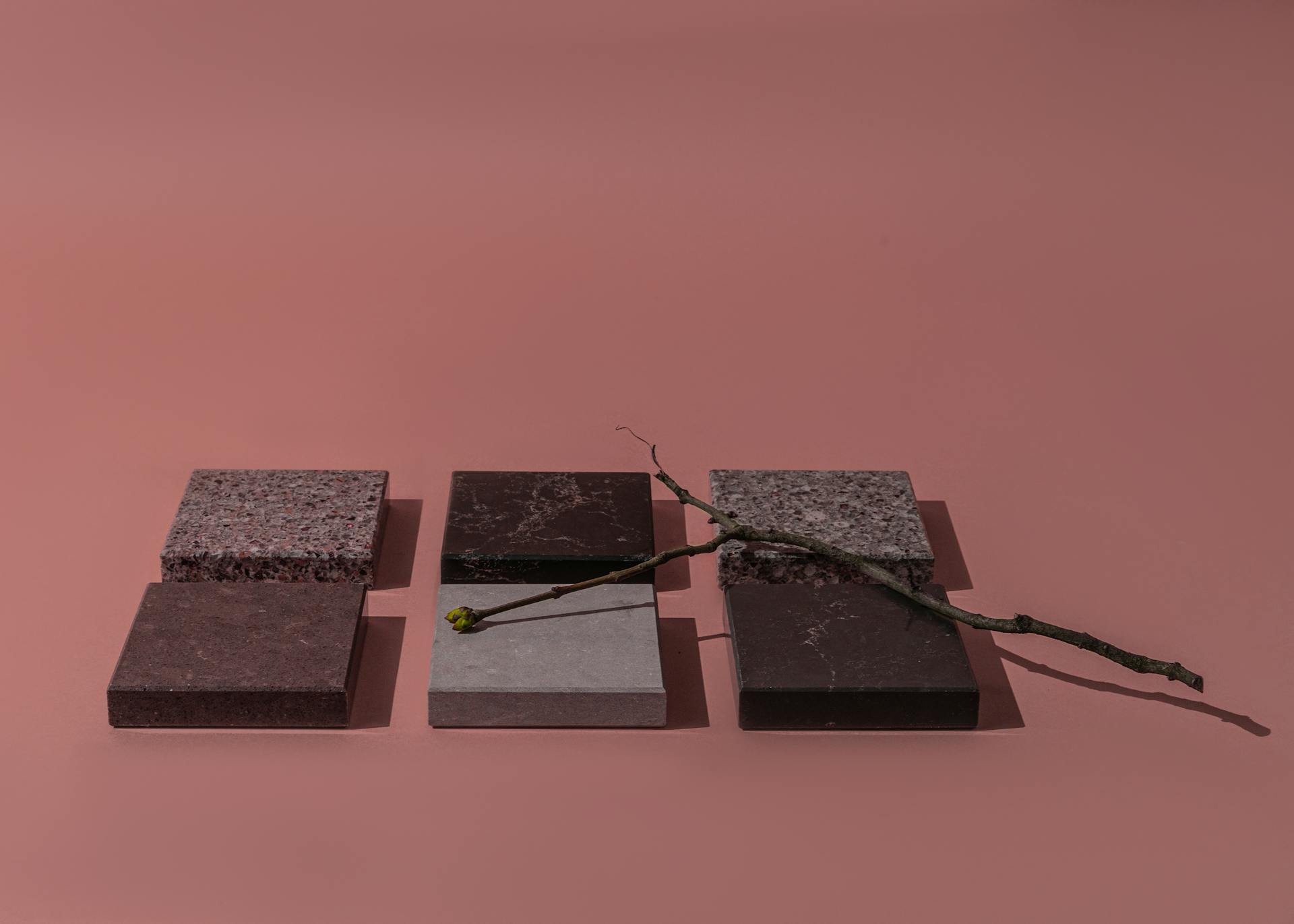 A minimalist arrangement of stone tiles and twig for a conceptual design on a pink backdrop.