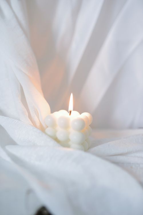 Free A lit bubble candle on soft white fabric, creating a soothing and warm atmosphere. Stock Photo
