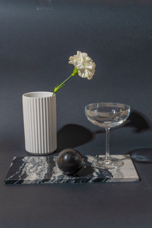 Free Elegant still life featuring a white flower in a vase, champagne glass, and sphere on marble. Stock Photo