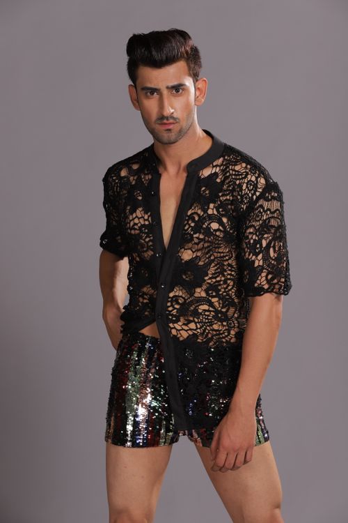 Free Male model posing in a studio wearing a lace top and sequined shorts, showcasing modern fashion. Stock Photo