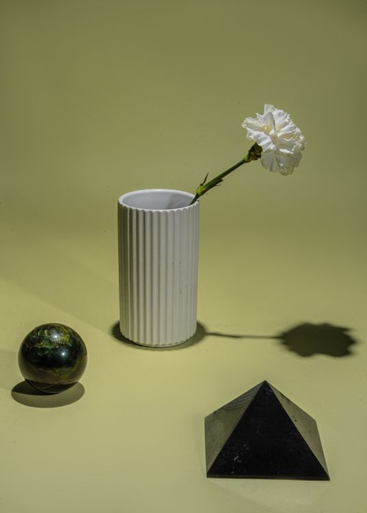 Free Artistic still life featuring a white vase, flower, sphere, and pyramid on a green background. Stock Photo