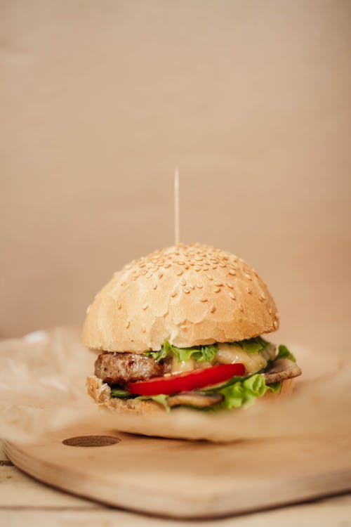 Tasty burger with juicy patty and tomato slice between sesame seed buns with skewer on parchment paper