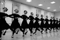 Black and white of crop graceful female dancers in flower head bands performing folkloric dance while looking away in room