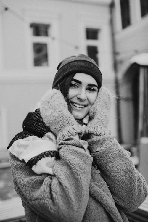 Smiling woman in warm clothes touching cheeks in town