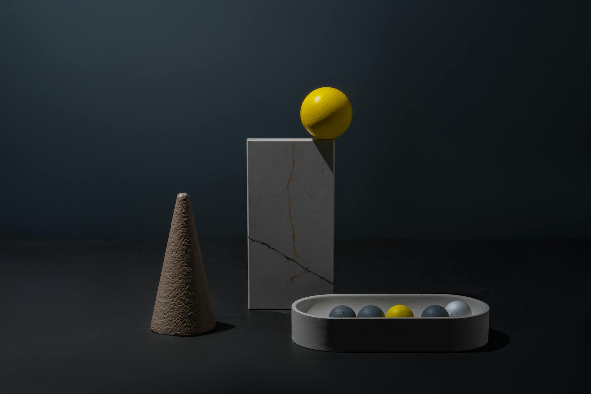 Artistic composition of geometric shapes with spheres and a cone against a dark background.