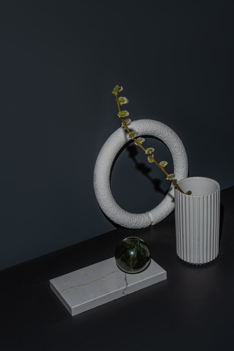 Jade Ball On A White Marble Next To A Porcelain Vase With A Twig And A Ring Stand