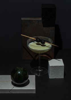 A stylish martini with olives in a glass, set against a dark abstract background.
