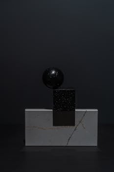 Minimalist geometric sculpture with cube and sphere on a dark background, perfect for design and art concepts.