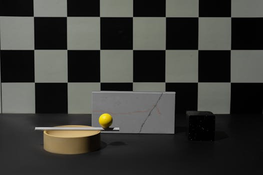A minimalist arrangement of geometric shapes featuring a yellow sphere against a checkered background.