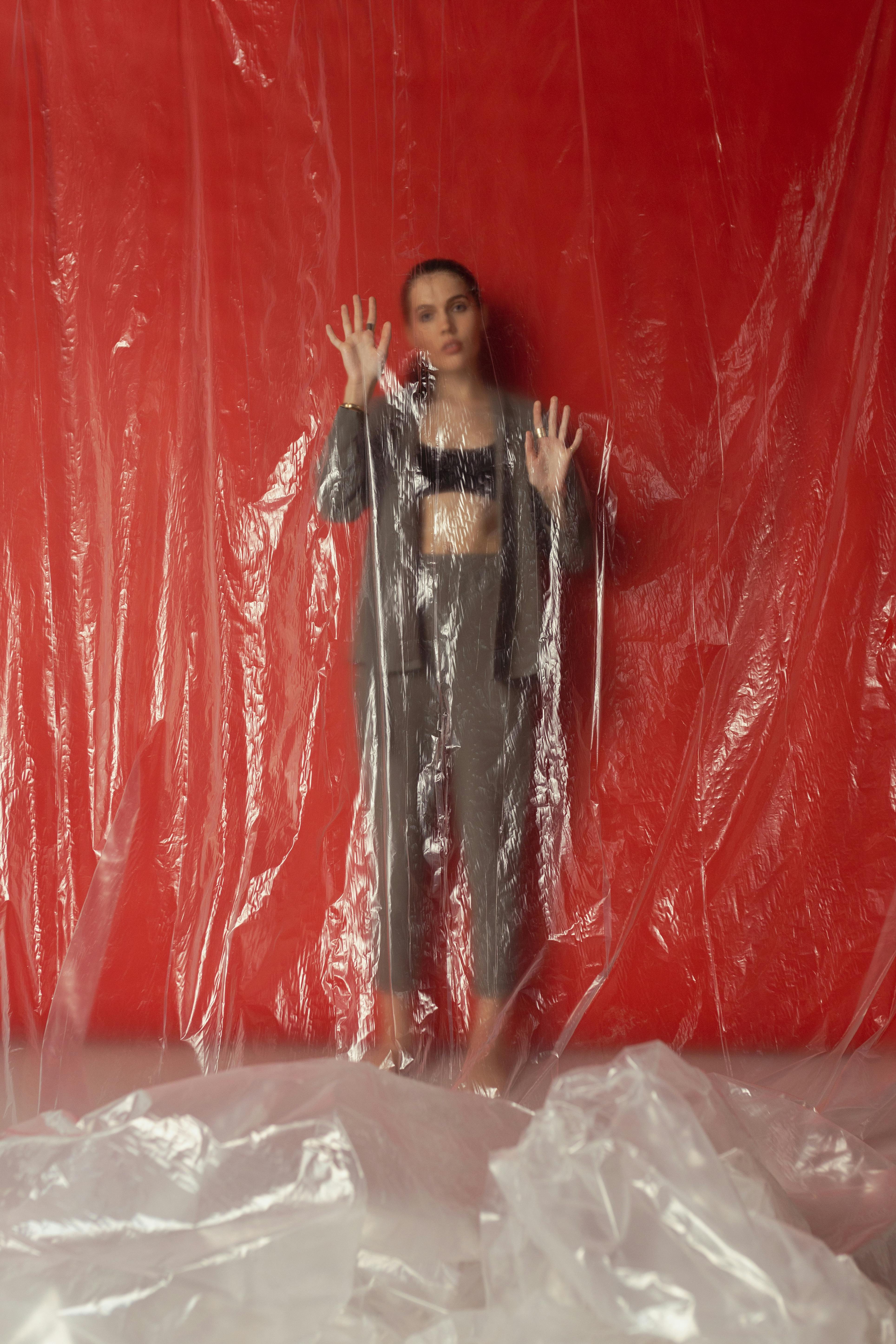 Woman in stylish outfit behind clear plastic against vivid red background.