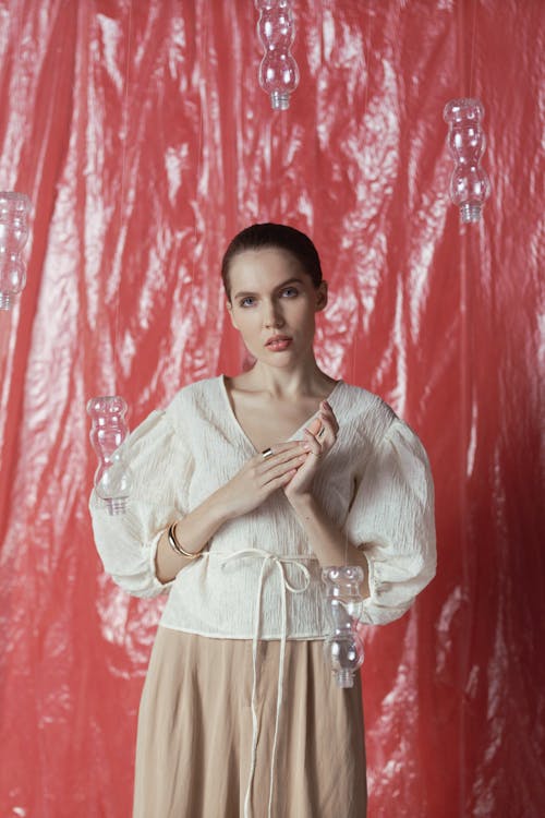 Woman in White Long Sleeve Shirt and Beige Skirt Standing Beside Red Curtain