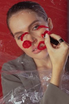 Artistic portrait of a woman applying red lipstick creatively on a clear surface.