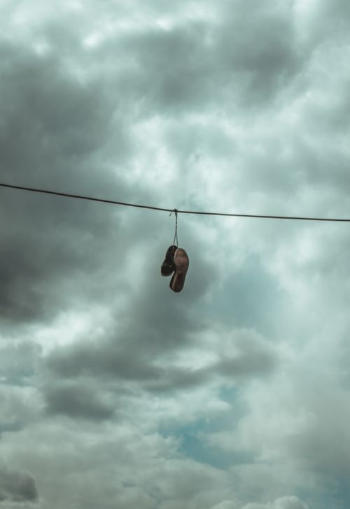 Free Pair of shoes dangling on a wire under a moody cloudy sky. Stock Photo