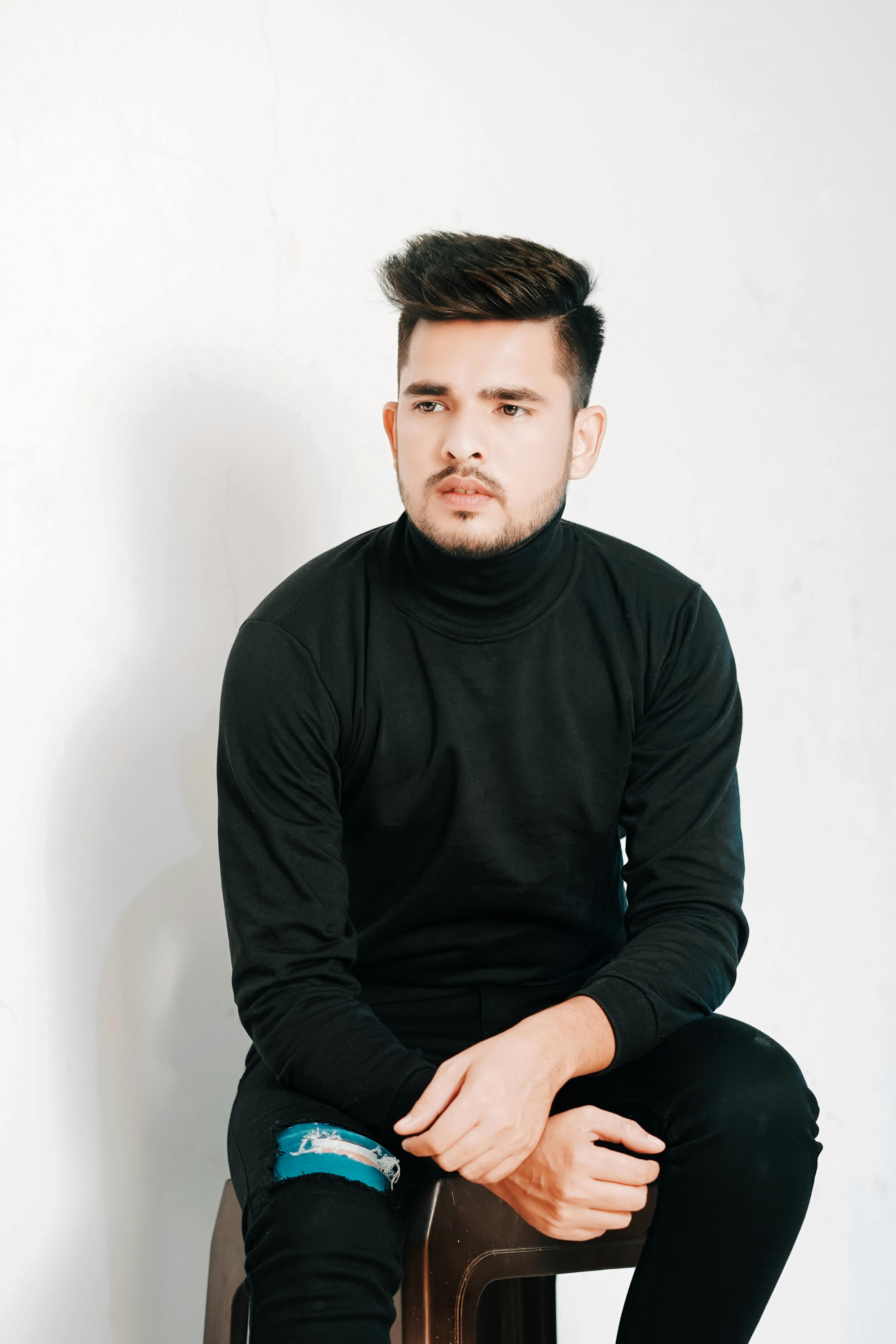 Studio portrait of a young man in a black turtleneck with modern hairstyle, sitting on a chair.