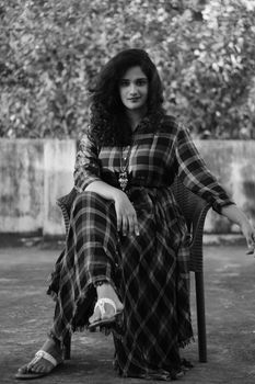 Black and white portrait of a woman seated outdoors in a plaid dress, exuding elegance.